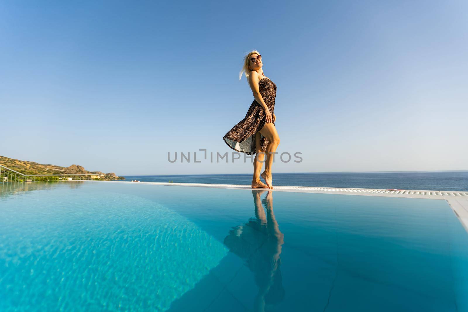 An attractive young woman stands near the pool with a panoramic view. by Andelov13