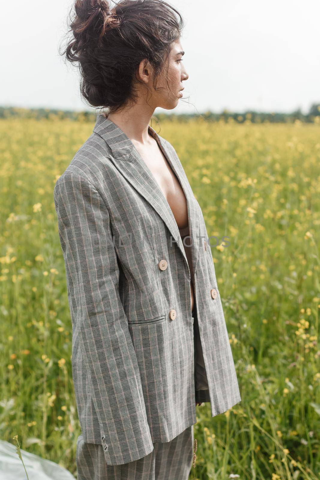 An Asian model poses in a field of yellow flowers for a clothing brand, polyethylene is the main props for a photo shoot. The concept of manufacturing clothing from recycled plastic. A woman in a pantsuit is standing on a plastic bag.