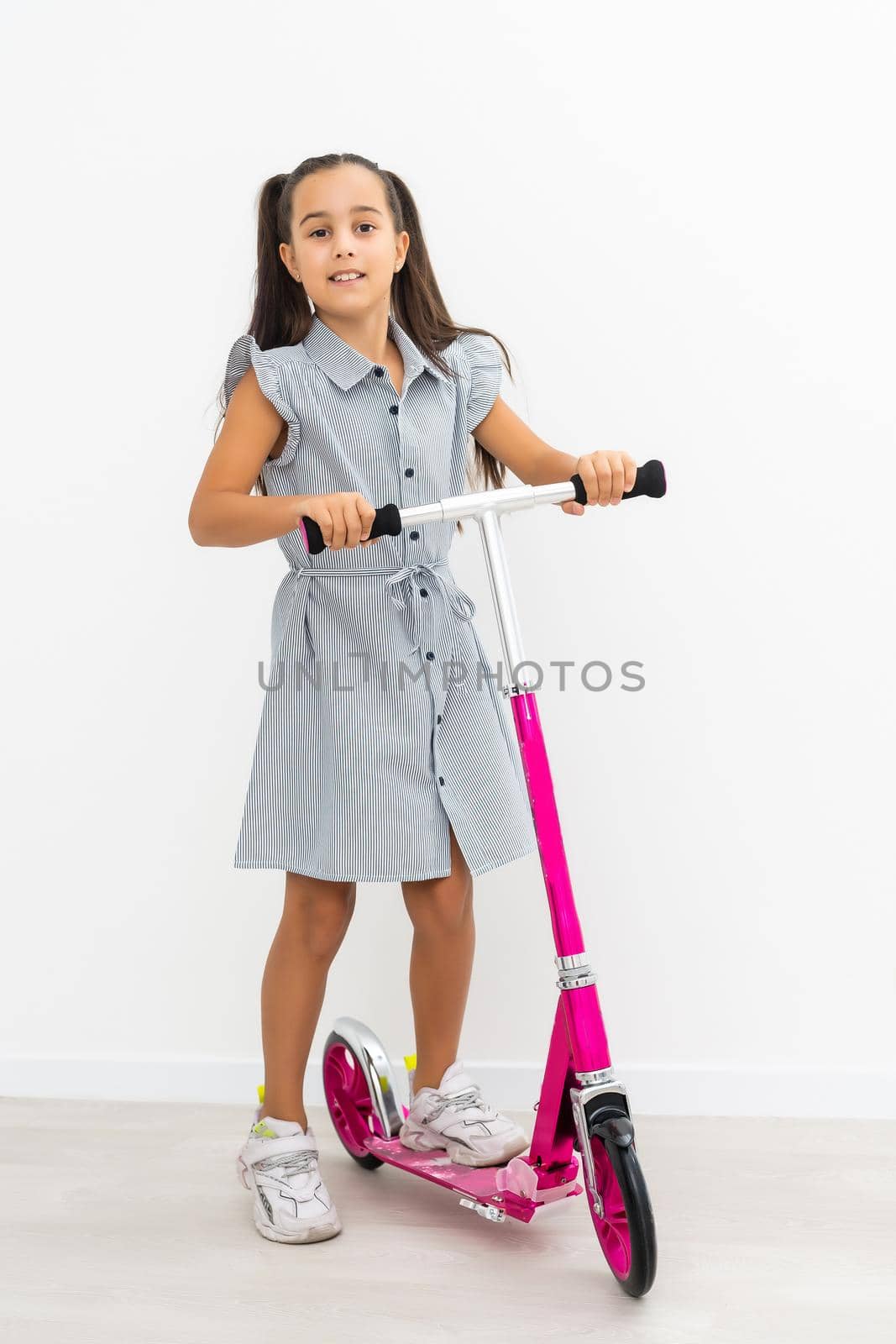 Happy little girl riding her scooter isolated on white