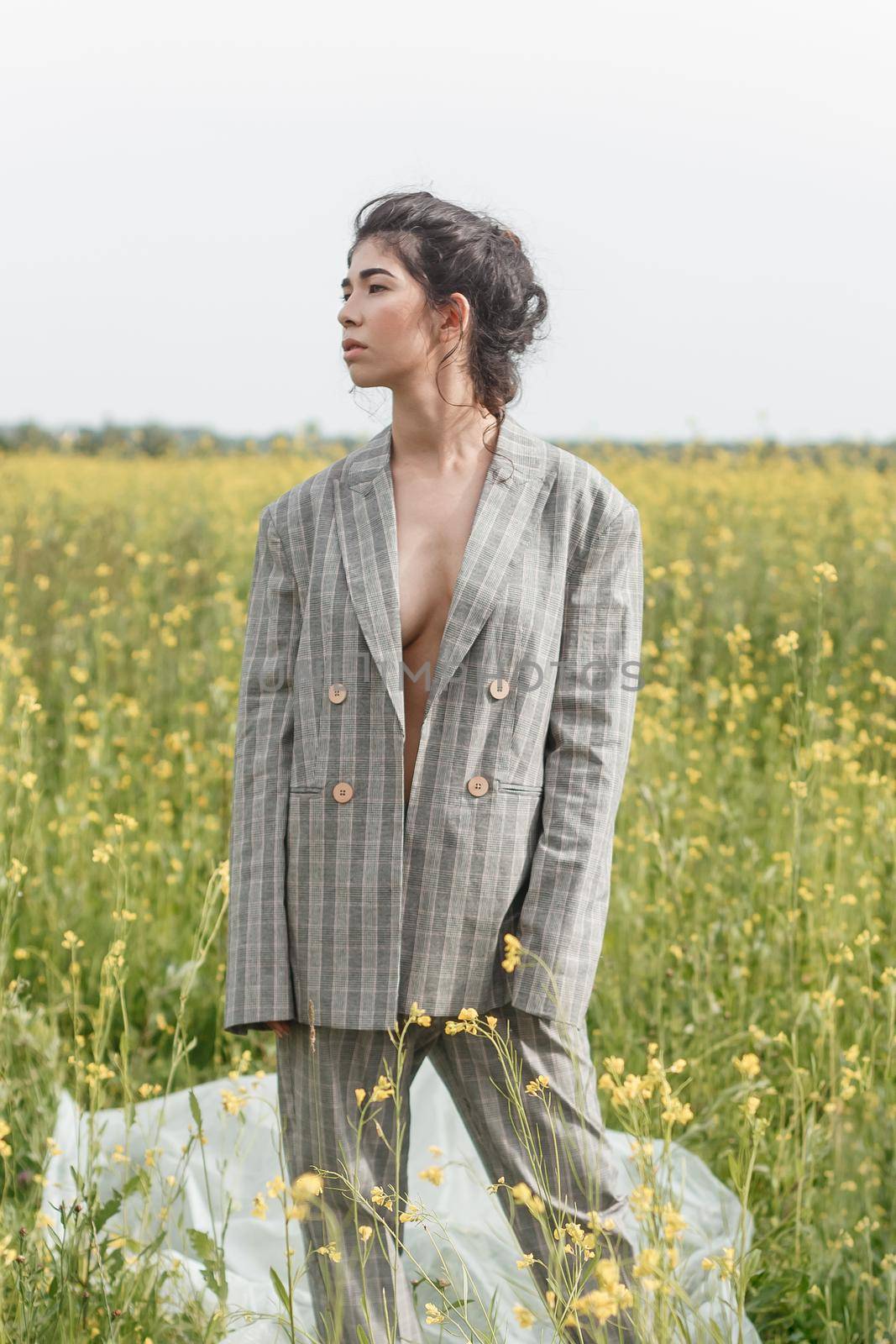 An Asian model poses in a field of yellow flowers for a clothing brand, polyethylene is the main props for a photo shoot. The concept of manufacturing clothing from recycled plastic. A woman in a pantsuit is standing on a plastic bag.