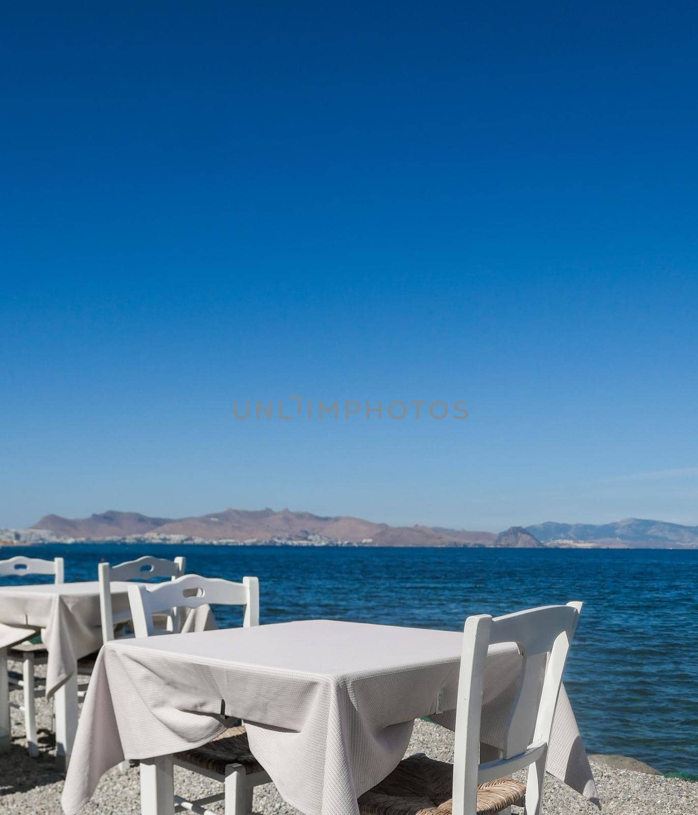 White restaurant tables on the beach in summer - travel, vacation and summer concept. The perfect lunch with a sea view