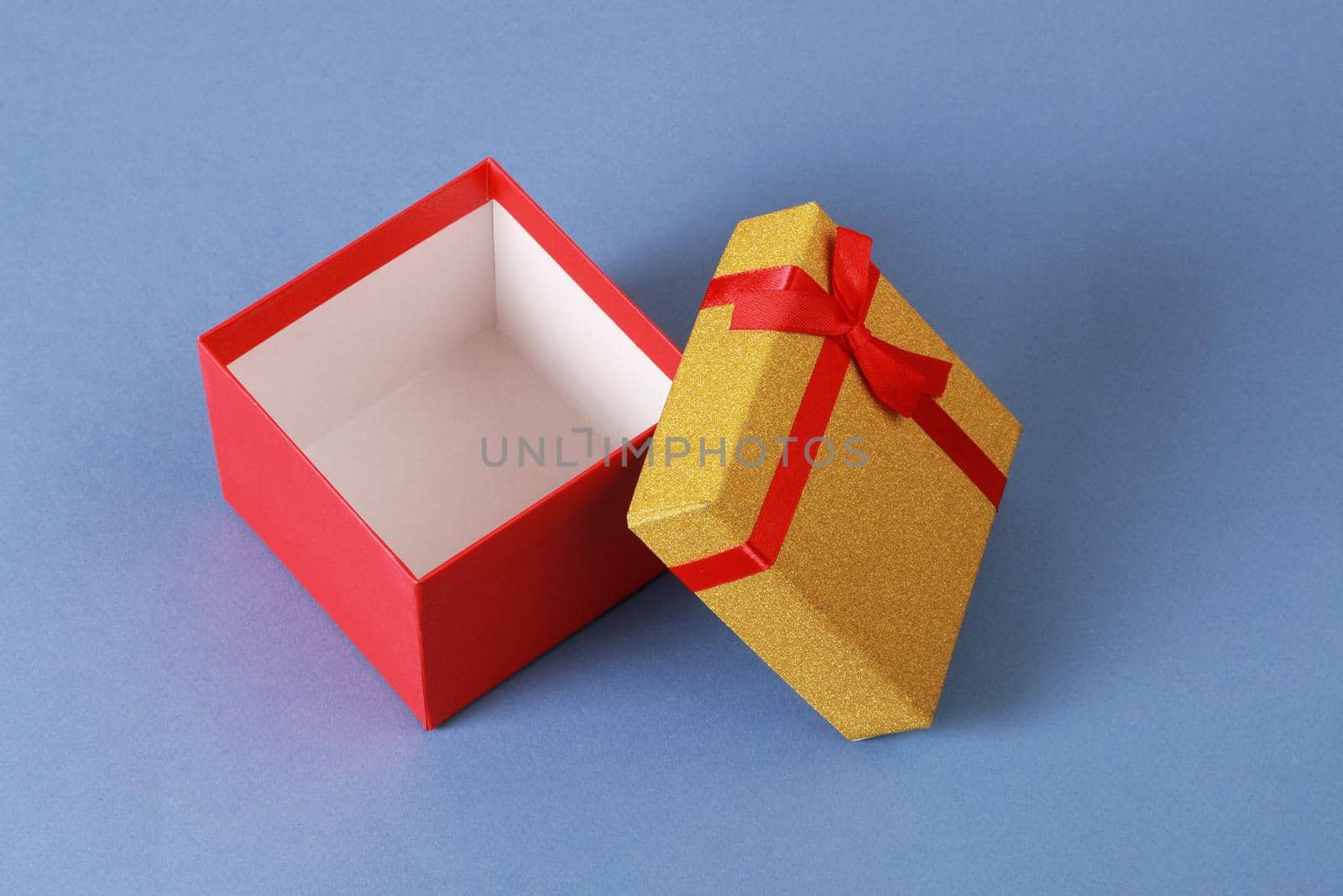 Red gift box. Yellow lid. Closeup of gift box on blue background.Birthday, valentine, anniversary or other holidays.