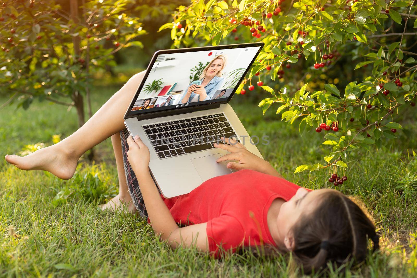 Beautiful young lady is chatting with friends outdoors as it is very useful to be in nature. Laptop is the best friend for a child nowadays. Green and vast meadow by Andelov13