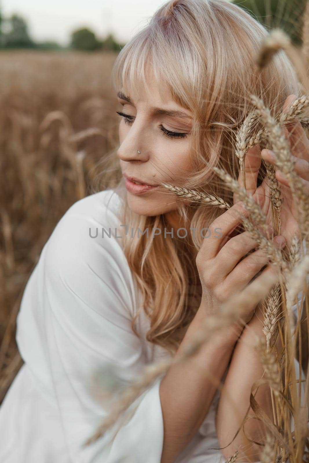 A blonde woman in a long white dress walks in a wheat field. The concept of a wedding and walking in nature.