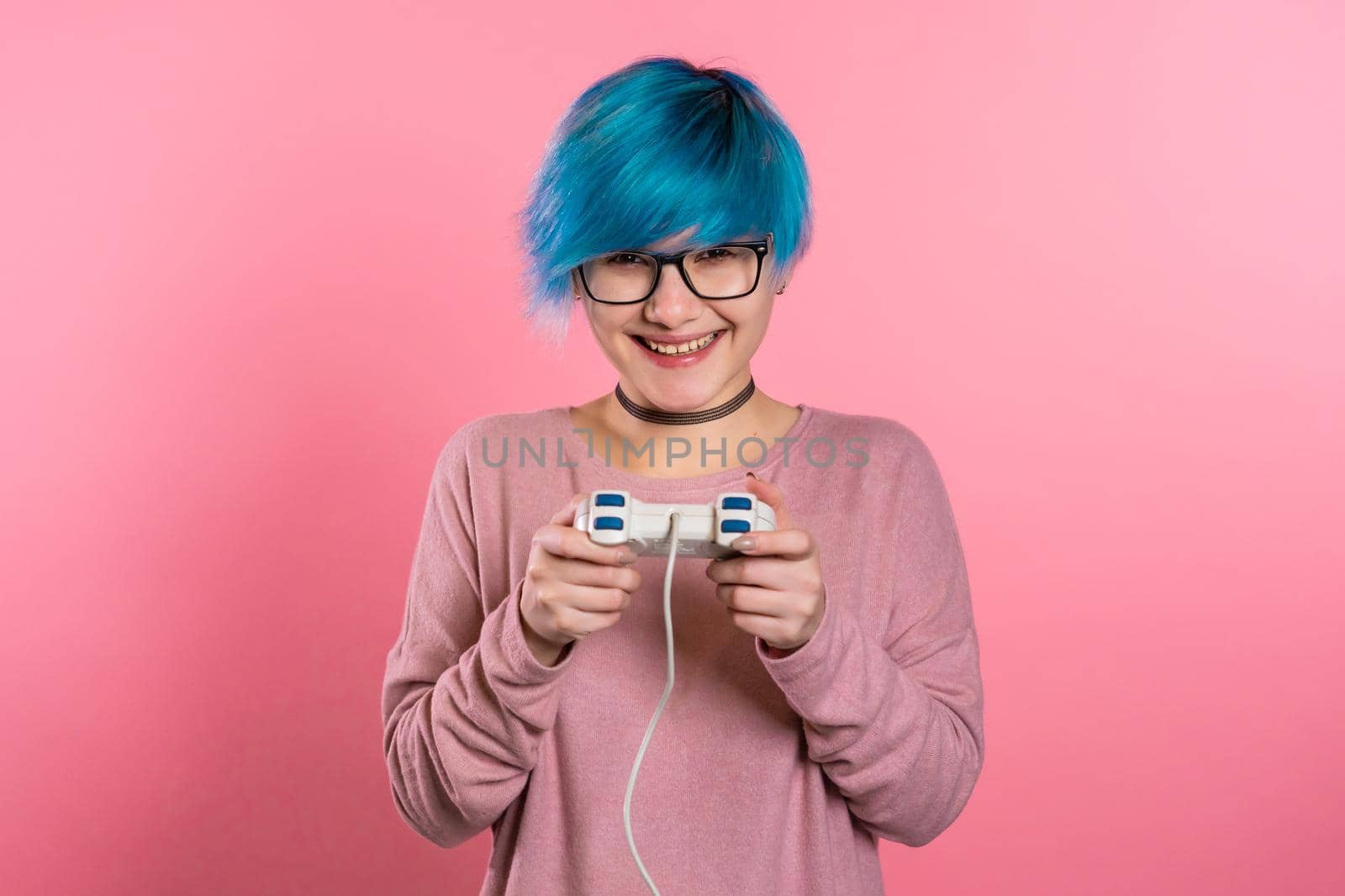 Pretty young girl with blue hairstyle playing video exciting game on Tv with joystick on pink studio wall. Using modern technology. by kristina_kokhanova