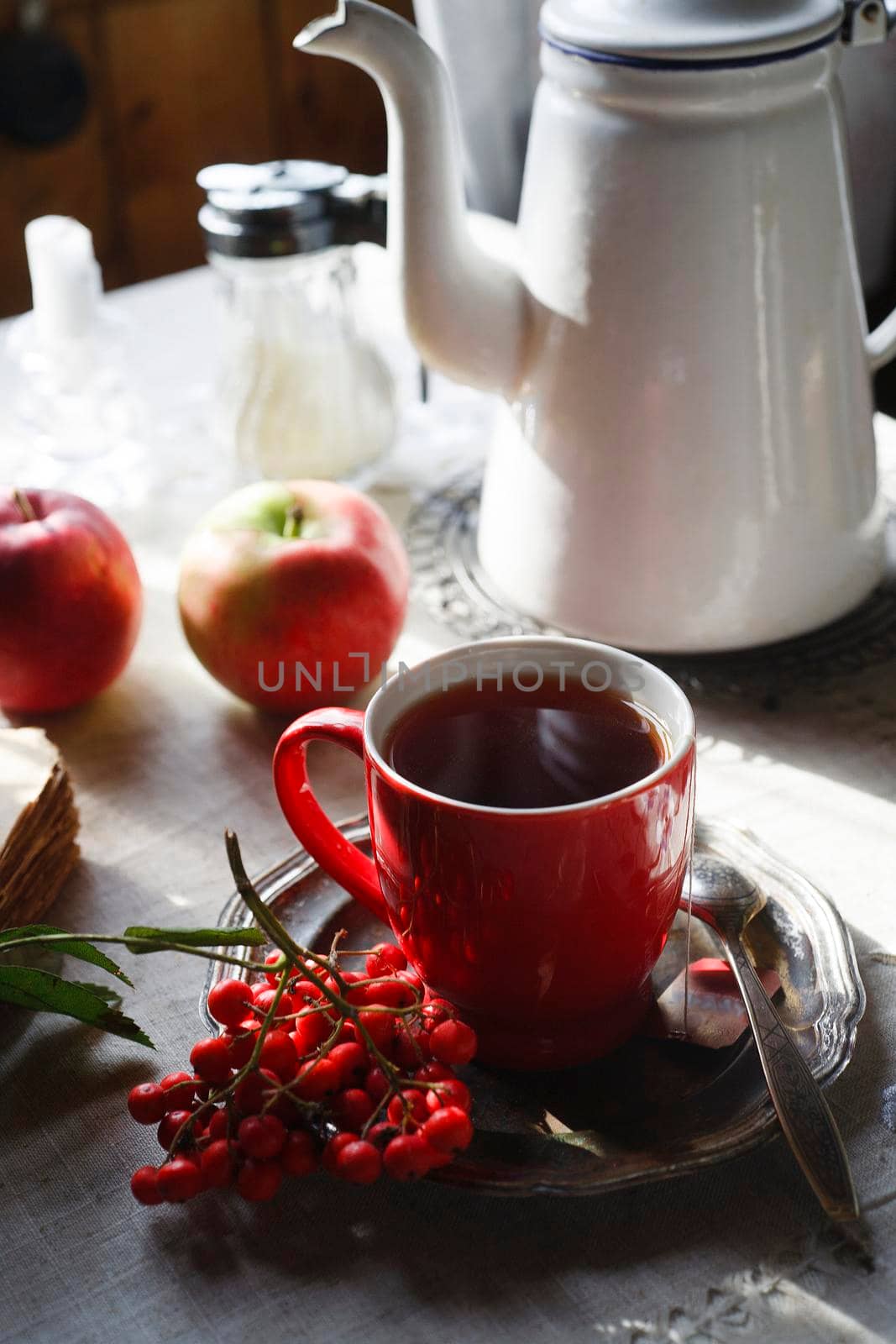 Red cup of tea on vintage metal plate with a bunch of red rowan and white tea pot, autumn morning tea concept, selective focus.