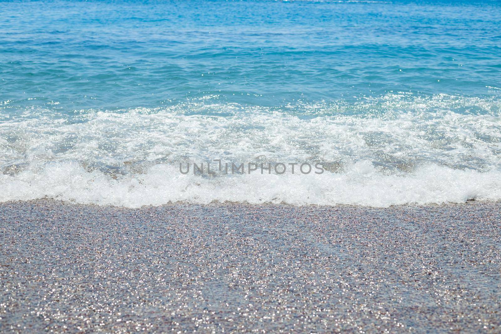 Pebble beach with azure sea water texture background