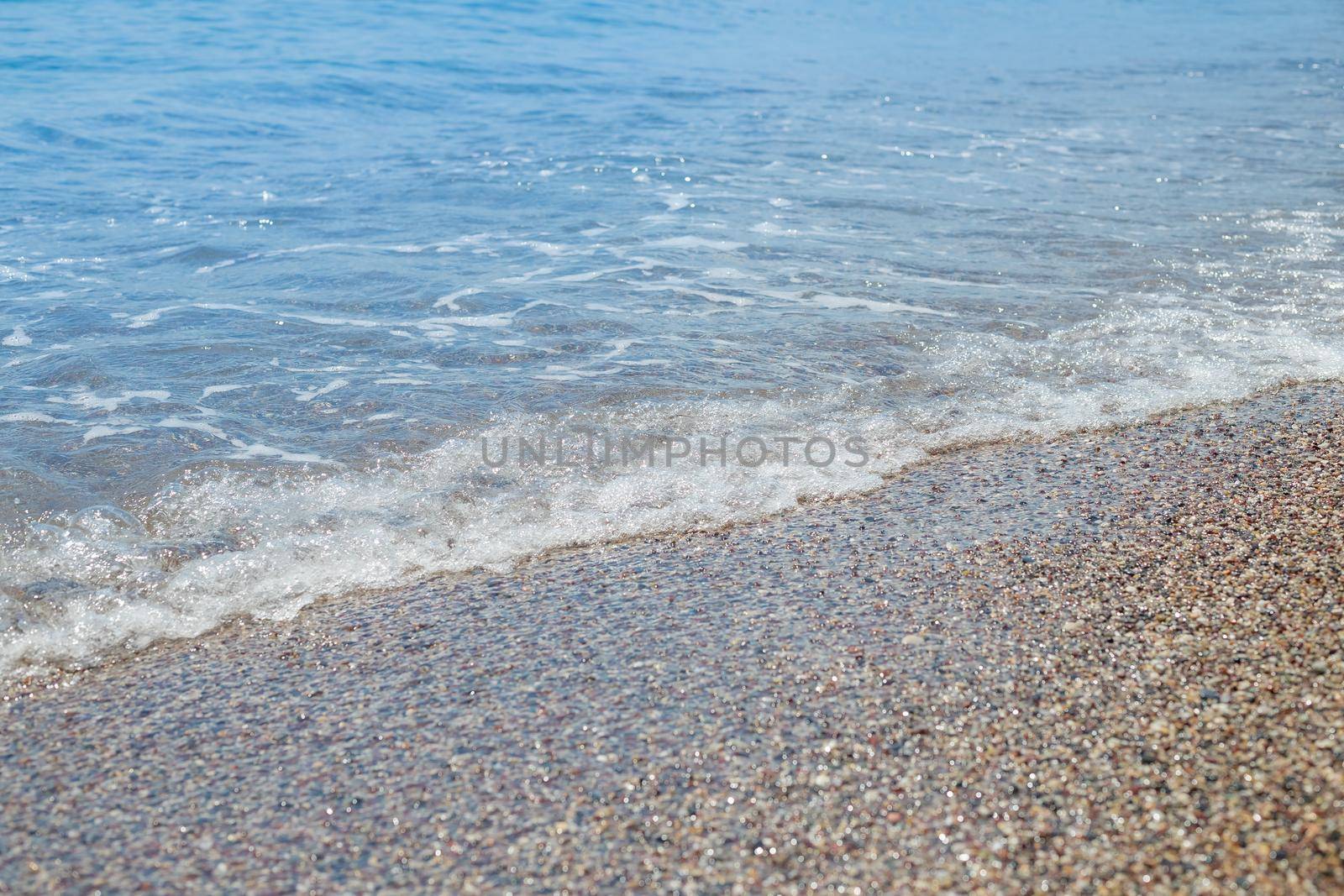 Pebble beach with azure sea water texture background