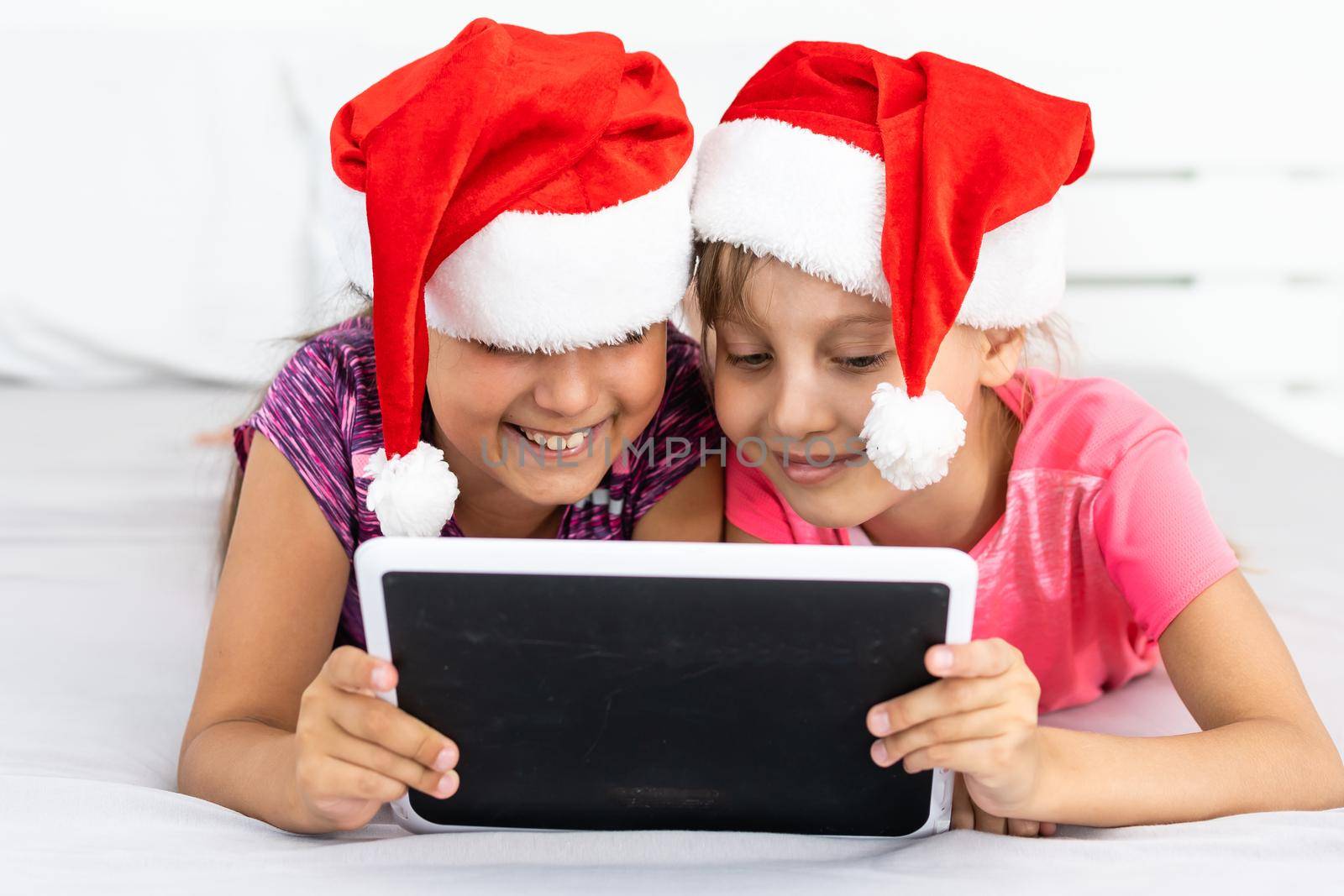 christmas, x-mas, winter, happiness concept - two adorable curly girls playing with tablet pc.