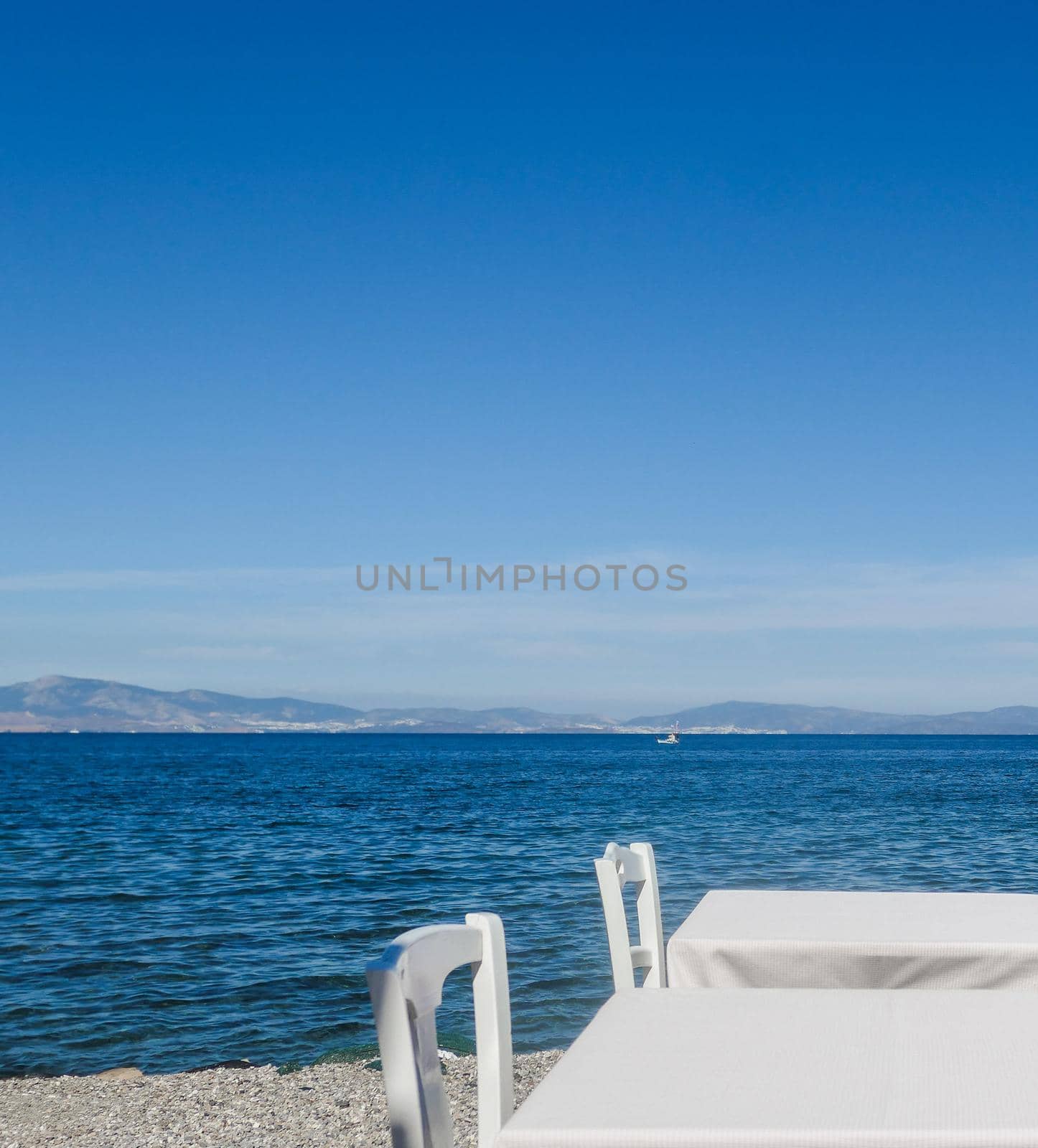 White restaurant tables on the beach in summer - travel, vacation and summer concept. The perfect lunch with a sea view