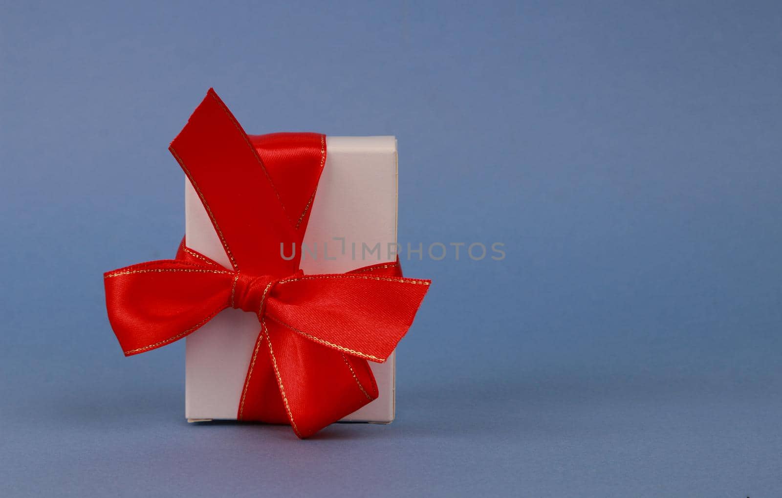 White paper box with a red bow on a blue paper background. Gift boxes with bow.