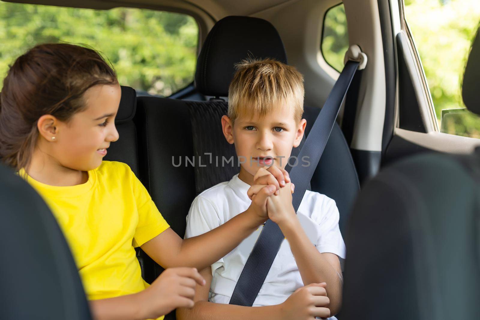Happy kids, adorable toddler girl with teenager brother sitting together in modern car locked with safety belts enjoying family vacation trip on summer weekend.