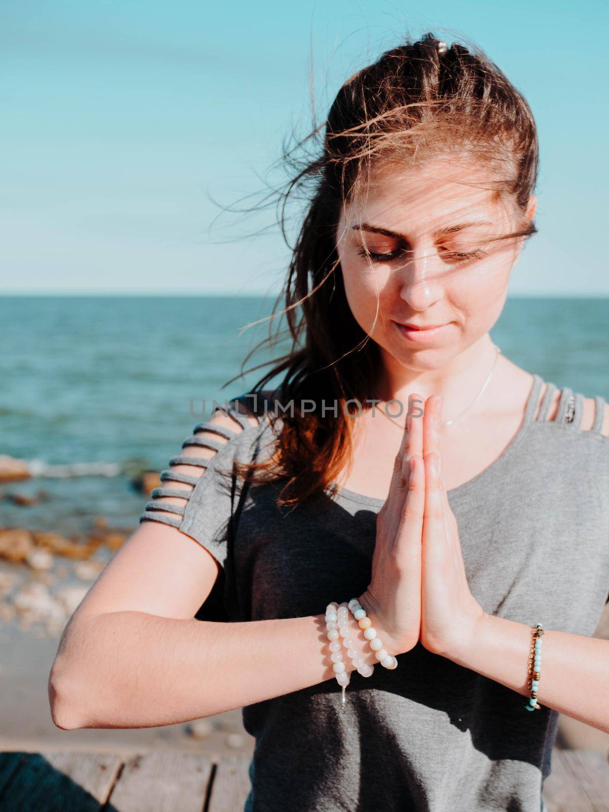 Young beautiful sporty woman doing yoga mudra on sea wooden beach near water. Girl practicing exercises. Hands in namaste. Gratitude sign. Health concept. High quality photo