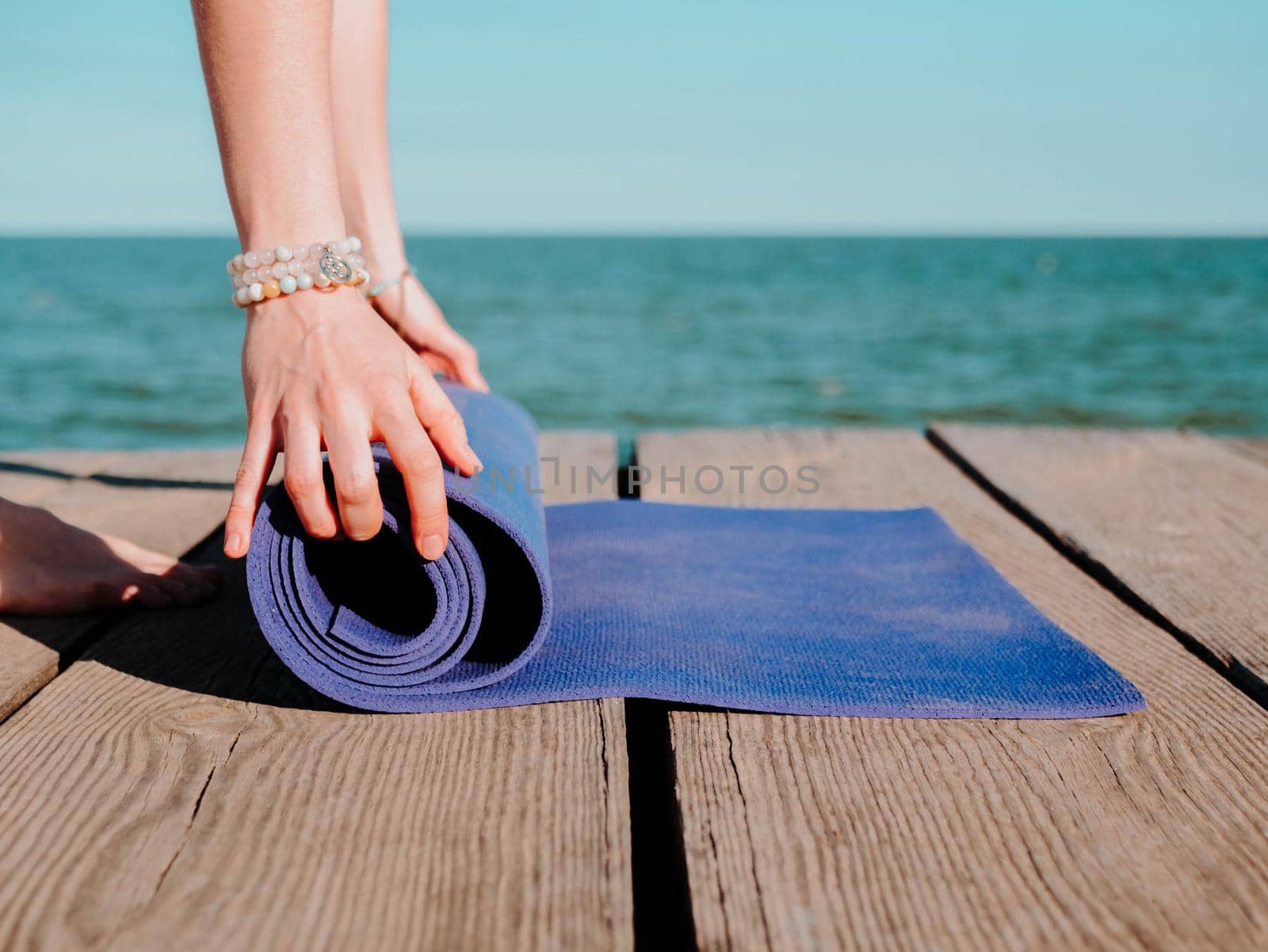 Young beautiful sporty woman preparing for yoga asana on sea beach near water. Girl covering purple mat. Health concept. by kristina_kokhanova