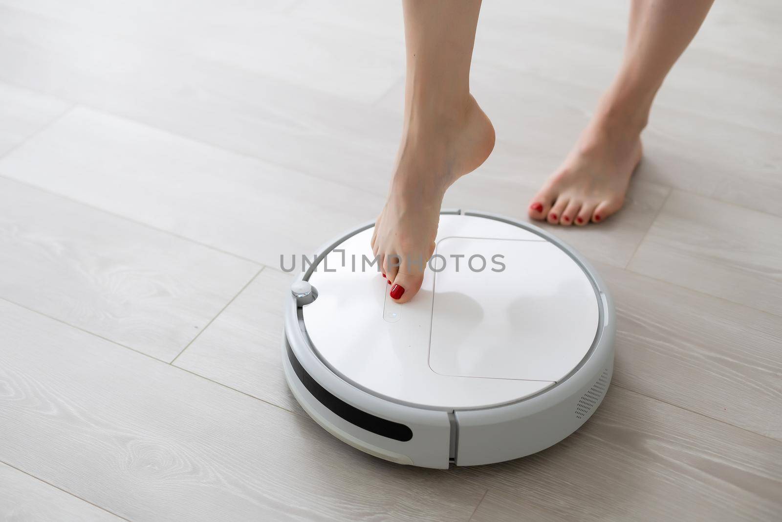 Human leg using smart robotic technology vacuum cleaner cleaning floor tiles background. Closeup top view image.