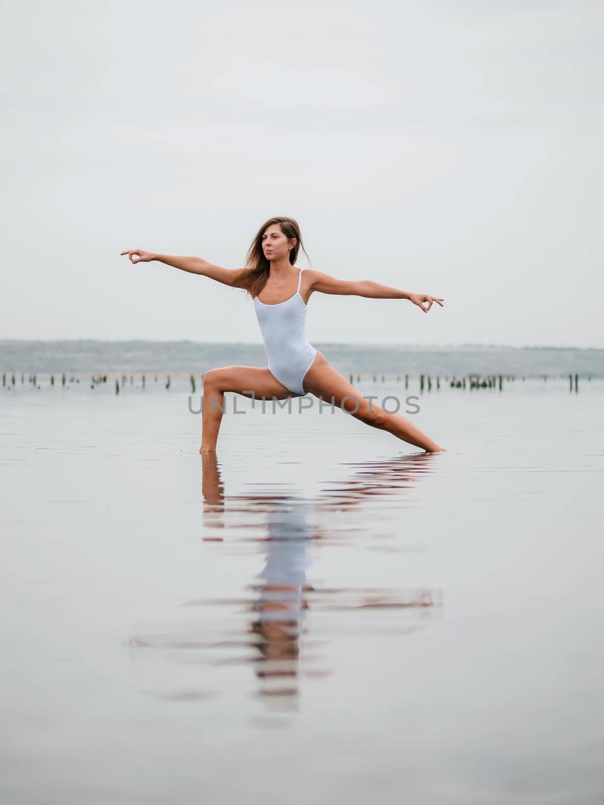 Young caucasian woman in swimsuit practicing yoga in water liman, lake or river. Beautiful reflection. Complex asanas, balance. Fitness, sport, yoga and healthy lifestyle concept. High quality photo