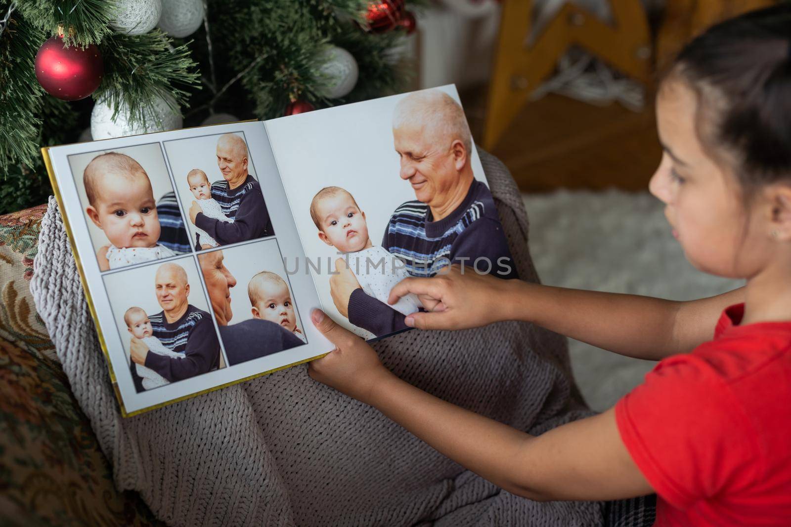 Little girl near the Christmas tree, with a photo book in her hands. Holiday decoration of the room, the Christmas tree