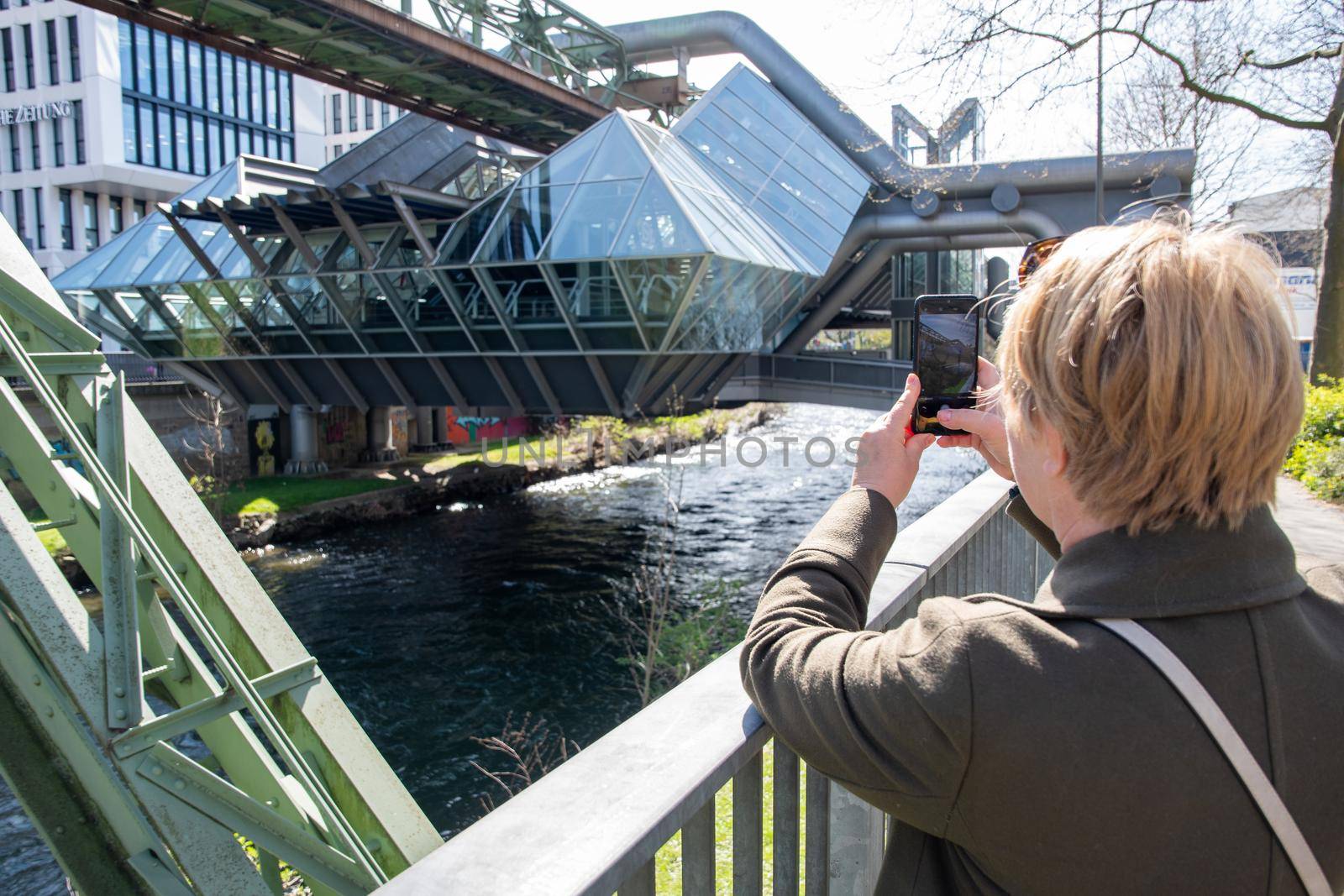 middle-aged blonde woman making a report of the Wuppertal Suspension Railway train in Germany, using mobile phone, The unique electric monorail system is landmark . High quality photo