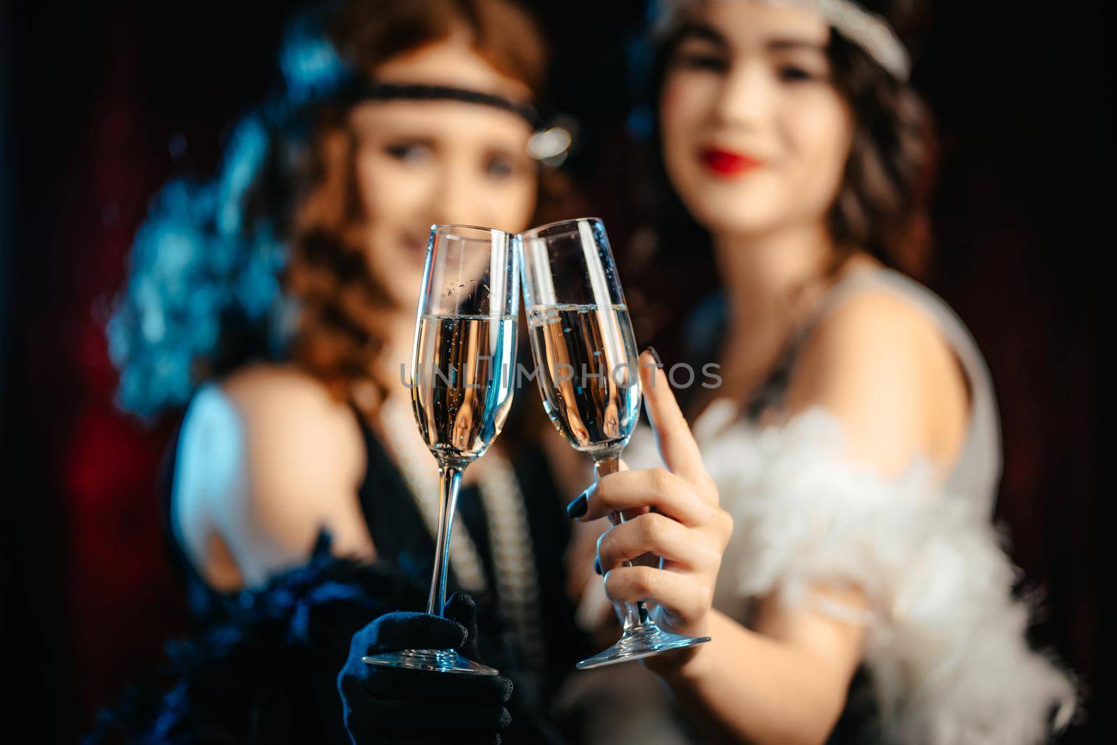 Close up glasses of champagne. Flappers women wearing in style of Roaring Gatsby twenties drinking alcohol. Vintage, retro party, fashion, girls friends concept. High quality photo