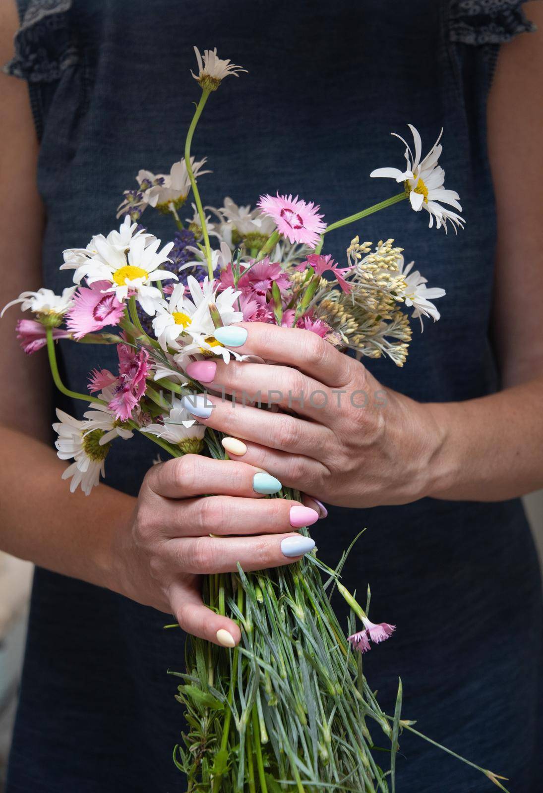 a young woman with a beautiful summer manicure holds a bouquet of wild flowers in pastel shades. High quality photo