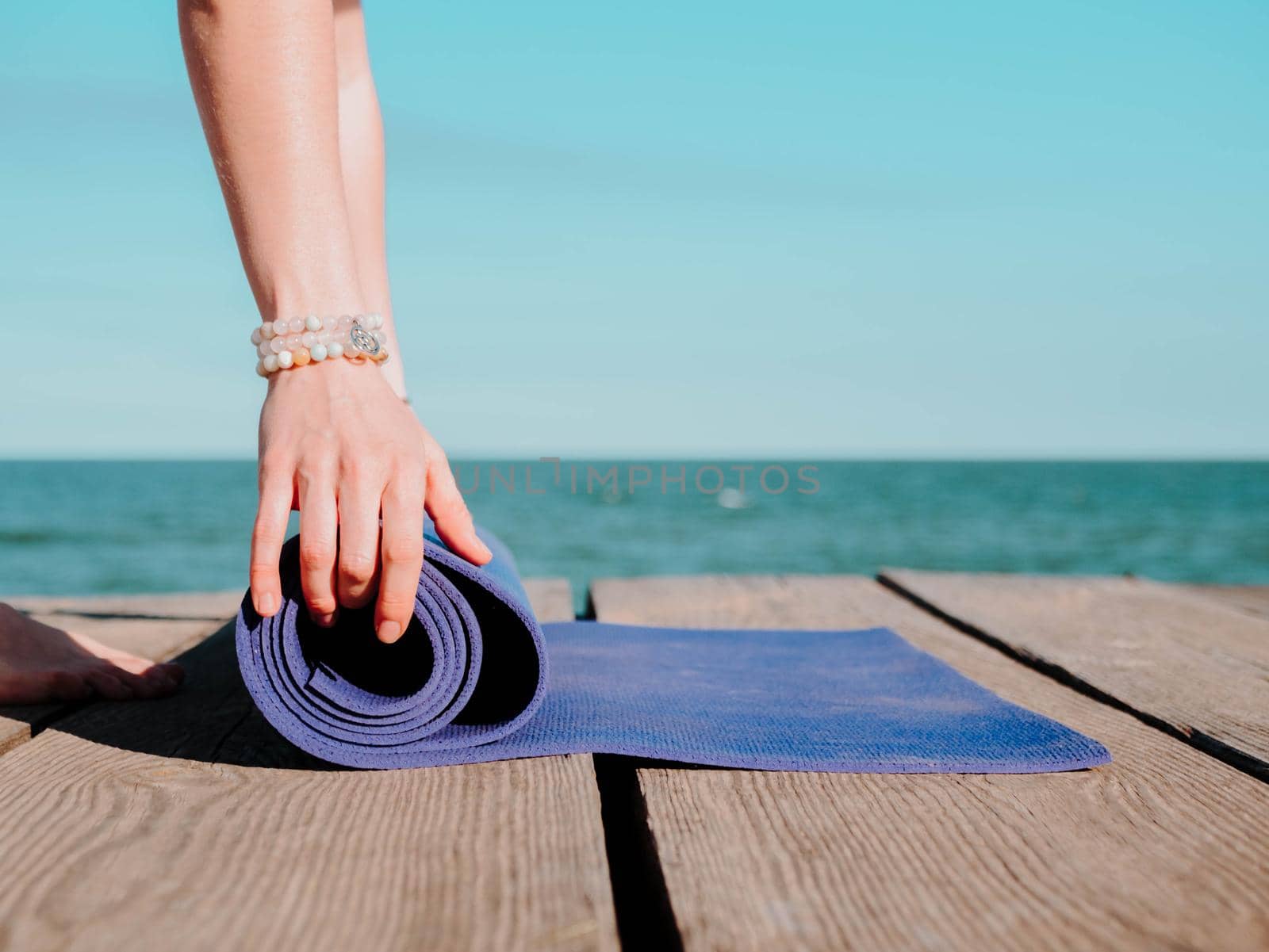Young beautiful sporty woman preparing for yoga asana on sea beach near water. Girl covering purple mat. Health concept. High quality photo
