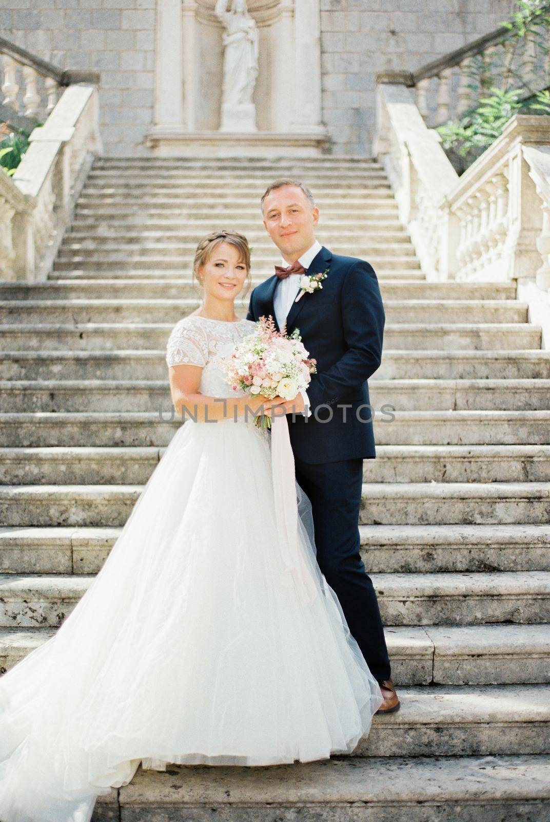 Groom and bride in a white dress stand on the stone steps. High quality photo