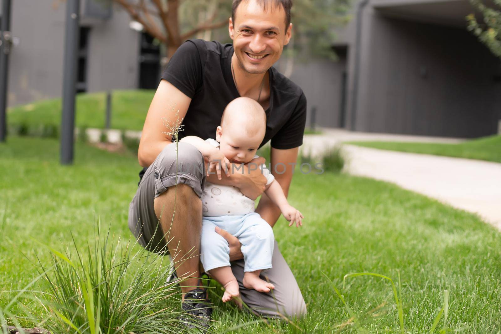 baby boy taking first steps with father help in a park.