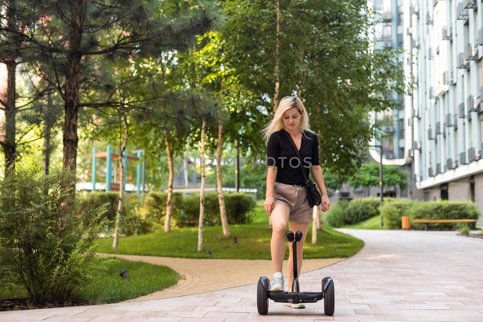 Back view of active tourist woman standing on electric self-balancing scooter at sunny park., young hipster girl driving on modern hover-board at holidays, blank space for design or content by Andelov13