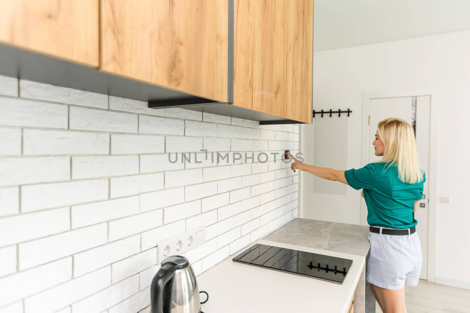 A woman is pressing the up button of a wall attached house thermostat with digital display showing the temperature. A concept image for electricity bill, heating, cooling, eco friendly, saving etc.