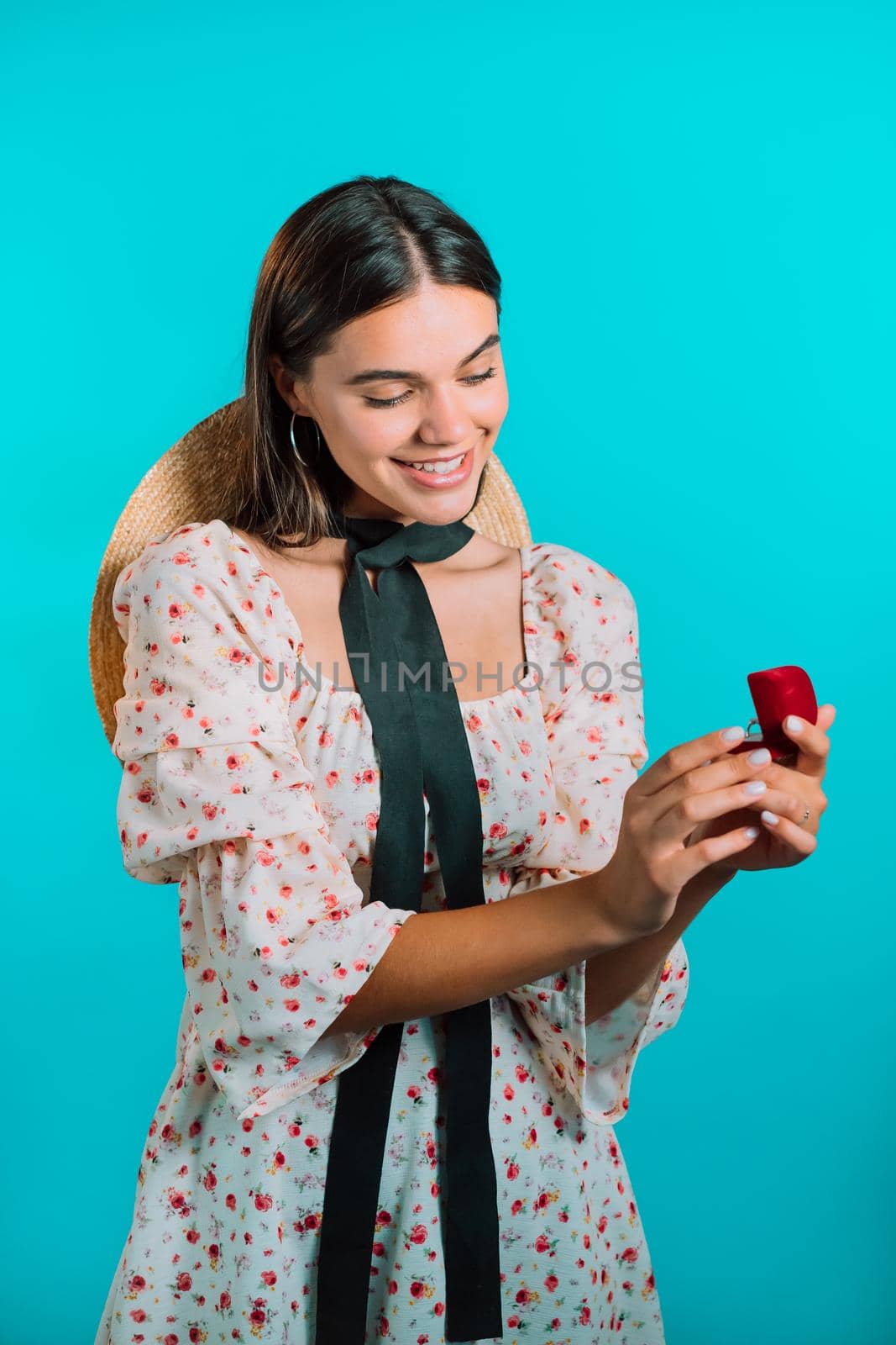 Attractive young woman holding small jewelry box with proposal diamond ring on blue wall background. Lady smiling, she is happy to get present, proposition for marriage.