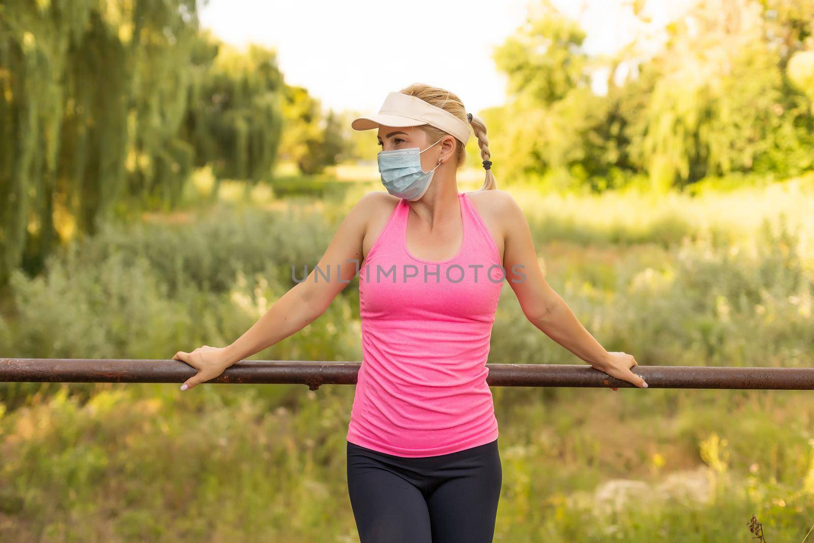Pandemic coronavirus COVID-19 A woman in a meadow in a sports outfit wearing a protective mask in case of the spread of SARS-CoV-2 disease virus. Girl with a protective mask on her face. by Andelov13