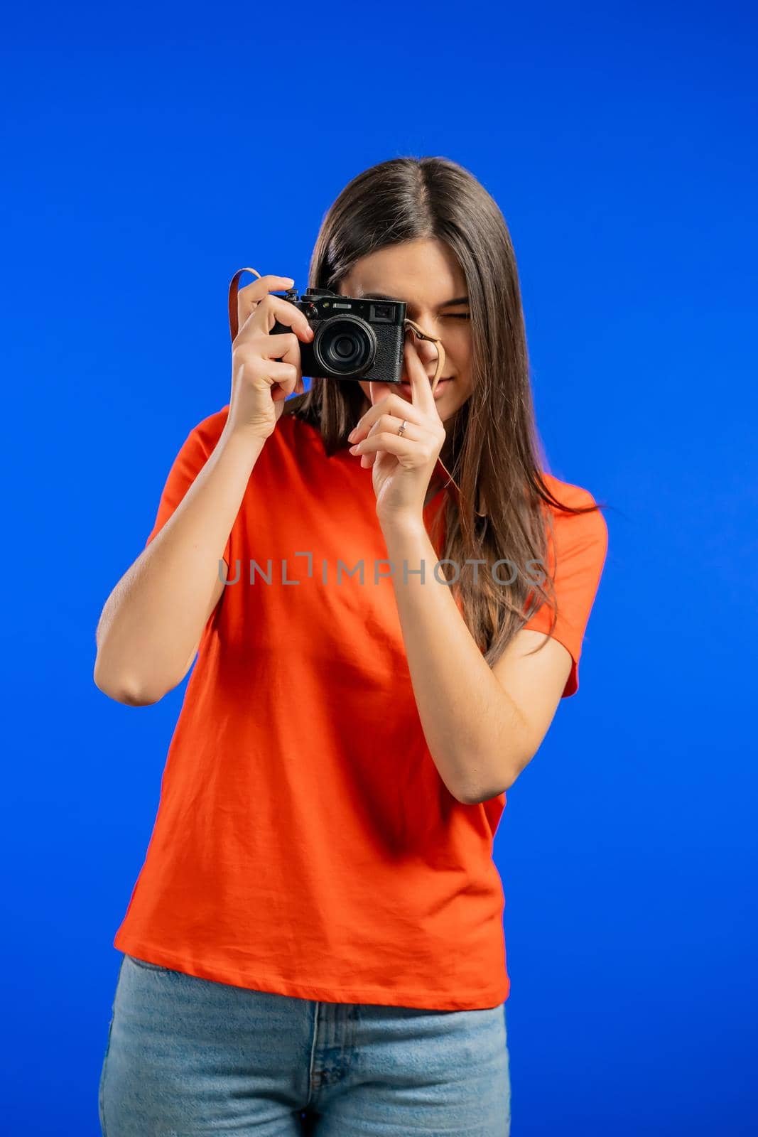 Young pretty woman takes pictures with DSLR camera over blue background in studio. Girl smiling as photographer. High quality photo