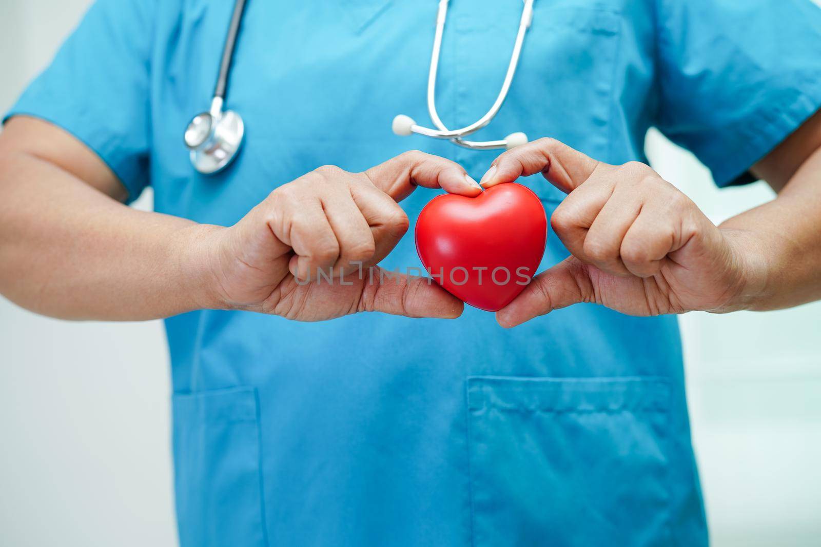 Asian woman doctor holding red heart for health in hospital.