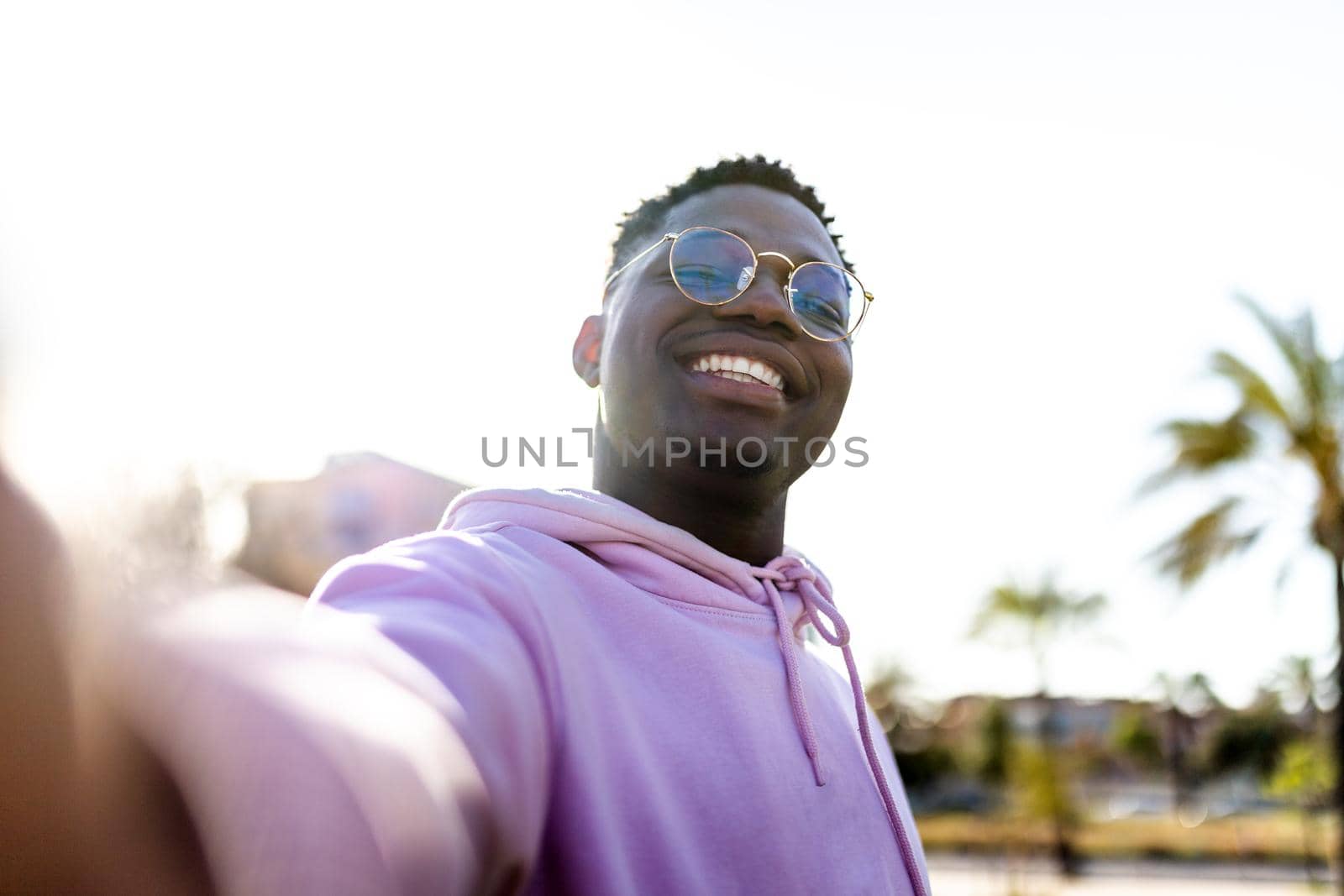 Happy African American man looking at camera taking selfie at the beach during vacations. Palm trees on background. Vacation concept.