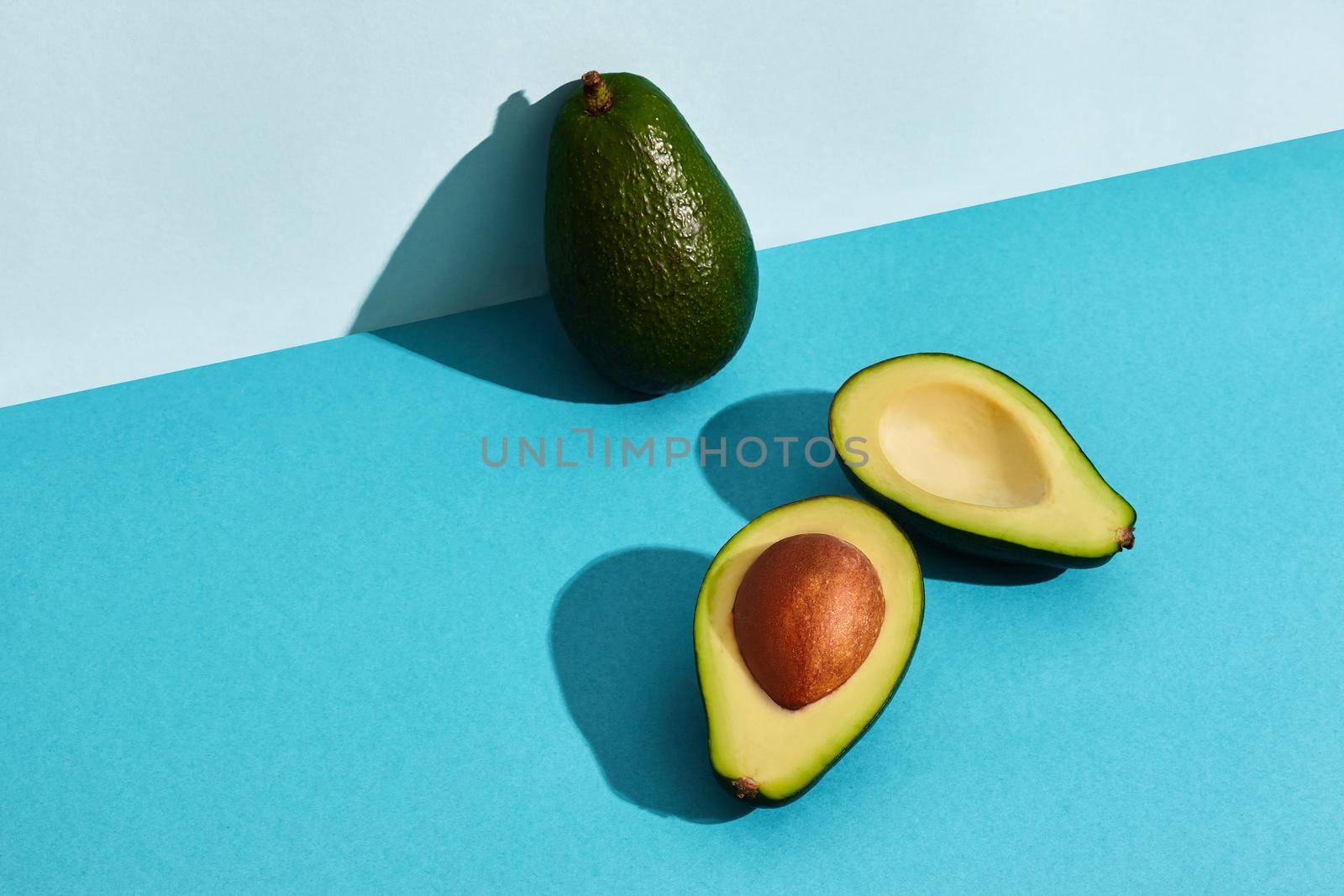 Composition of fresh fruits, whole avocado and two halfs of cutted avocado on blue background. Mock up, two-colored pastel