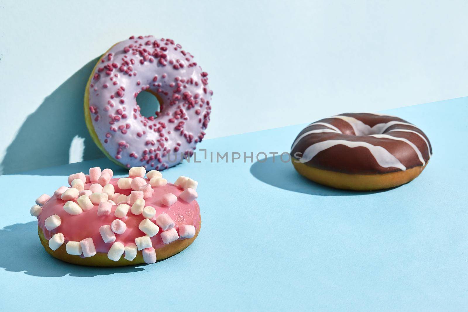 Close up photo of three sweet tasty donuts in caramel and chocolate icing, on a blue background. Mock up, two-colored pastel