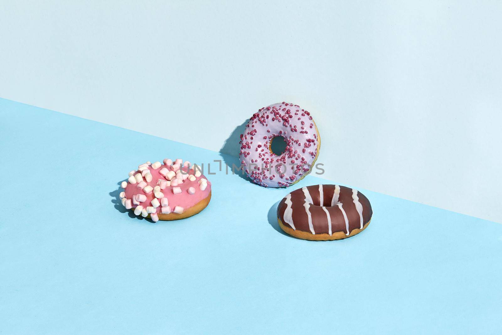 Three sweet tasty donuts in caramel and chocolate icing, on a blue background. Mock up, two-colored pastel