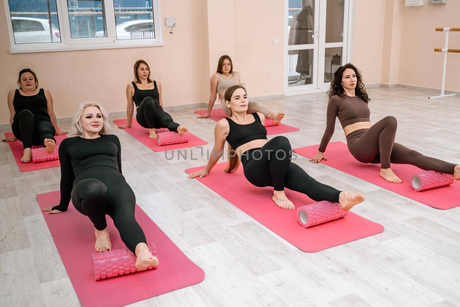 Athletic women doing fascia exercises on the floor with a foam roller massage tool to relieve back tension and relieve muscle pain. The concept of physiotherapy and stretching training.