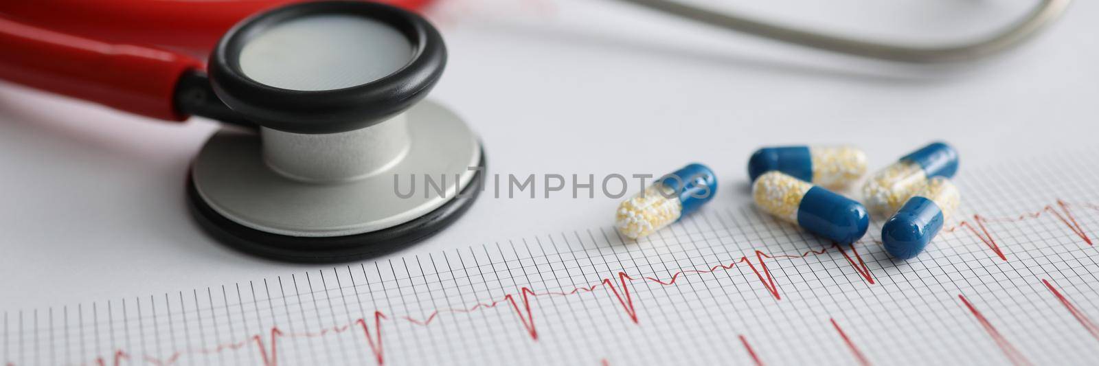 Medical capsules and red stethoscope lying on electrocardiogram closeup by kuprevich