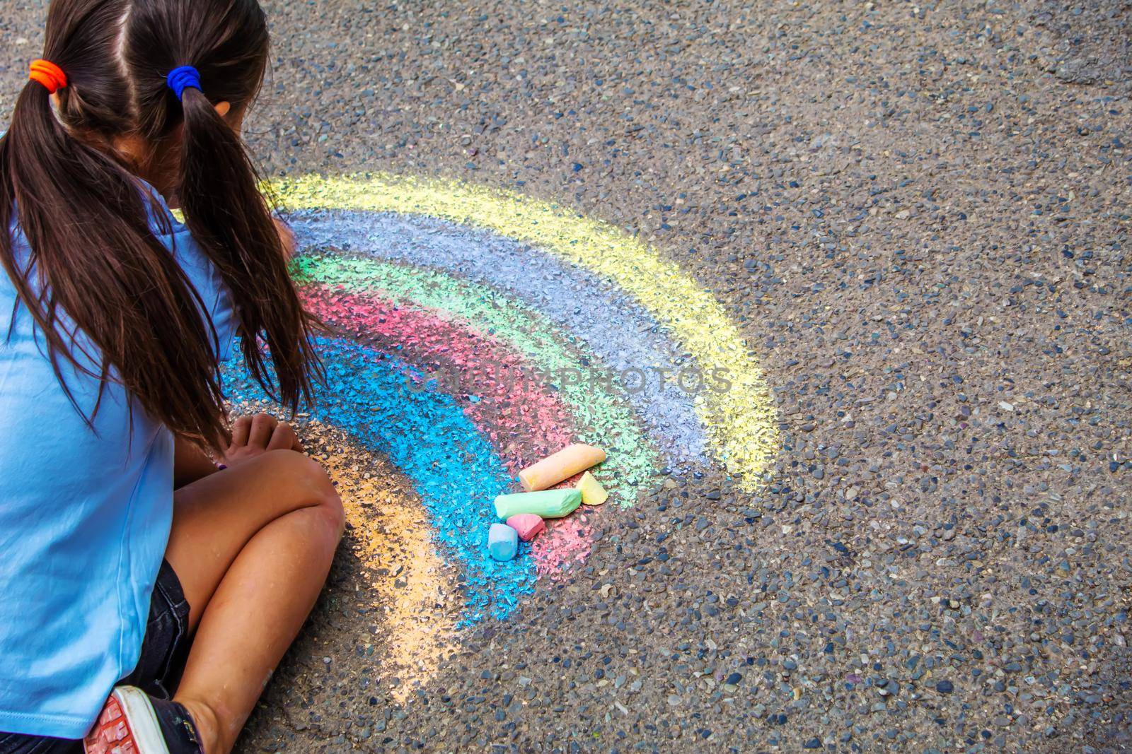 A child draws a rainbow on the asphalt. Selective focus. by mila1784