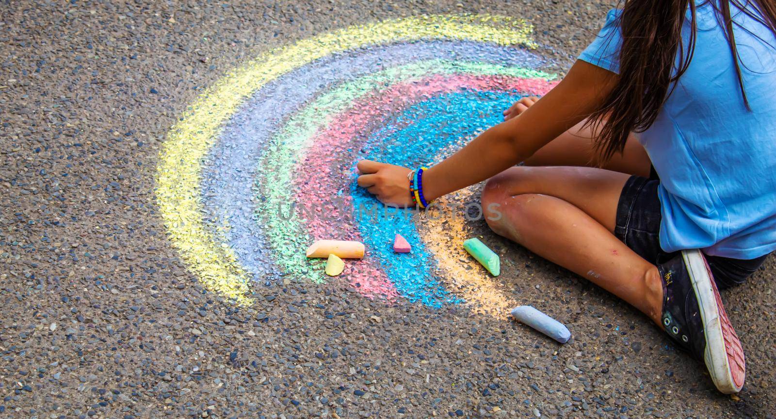 A child draws a rainbow on the asphalt. Selective focus. by mila1784