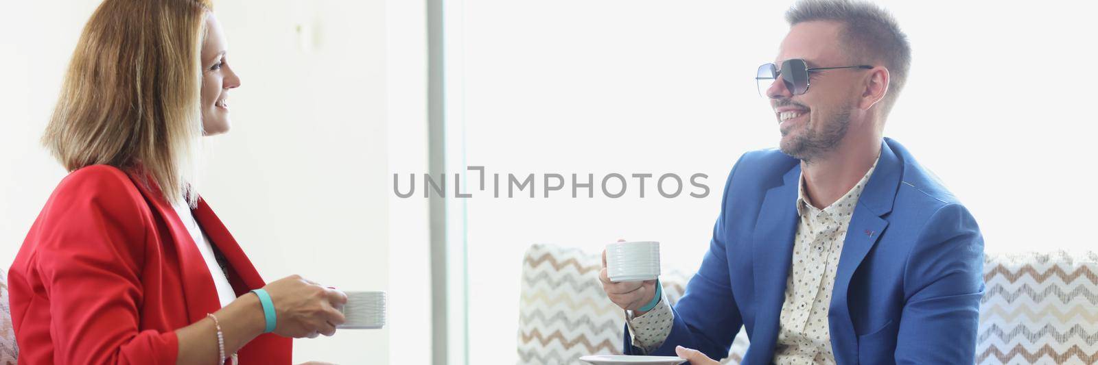 Young man and woman in business suits drinking coffee and chatting in cafe by kuprevich