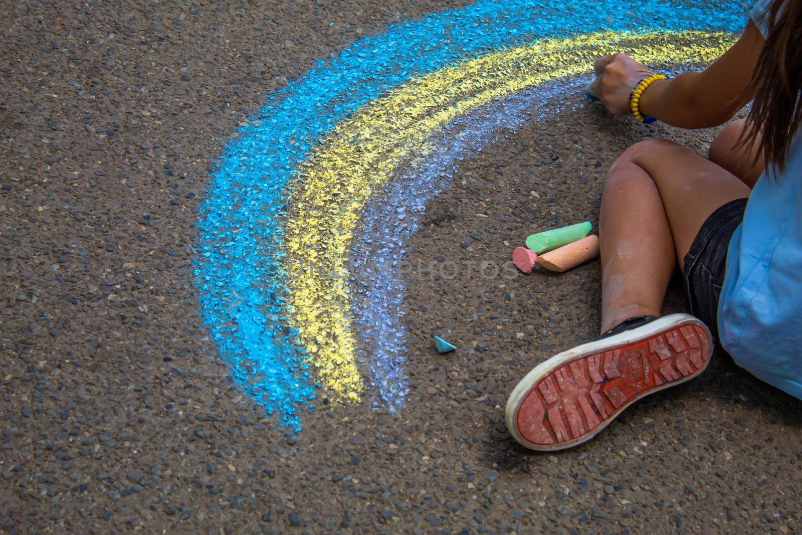 A child draws a rainbow on the asphalt. Selective focus. by mila1784