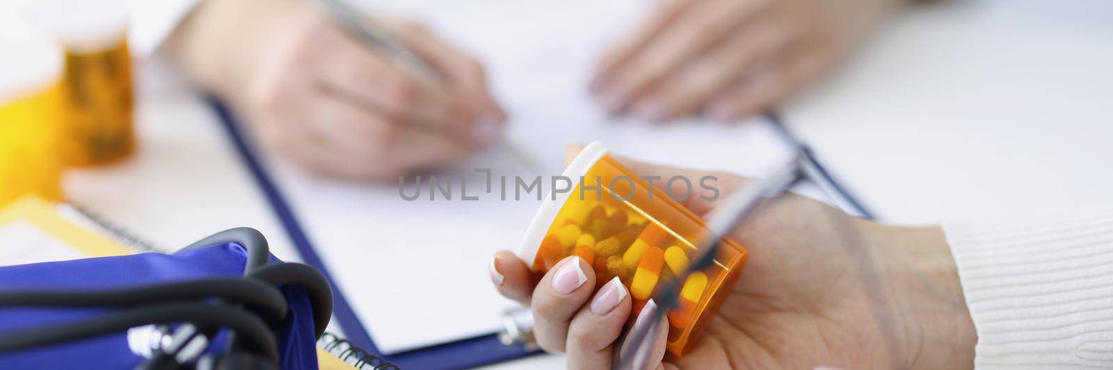 Patient holding jar of medicines in his hands against background of doctor closeup. Prescription drug dispensing concept