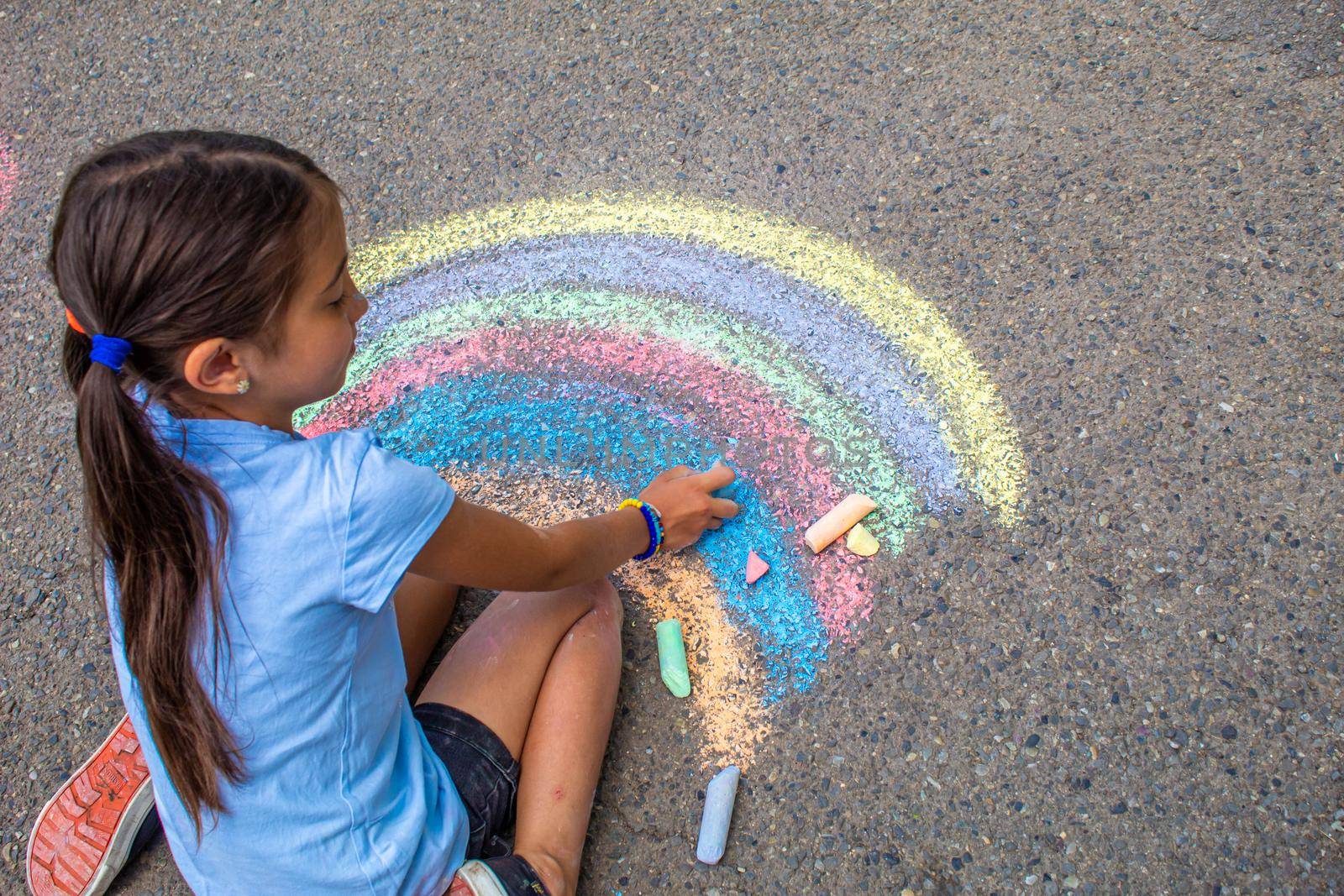 A child draws a rainbow on the asphalt. Selective focus. by mila1784