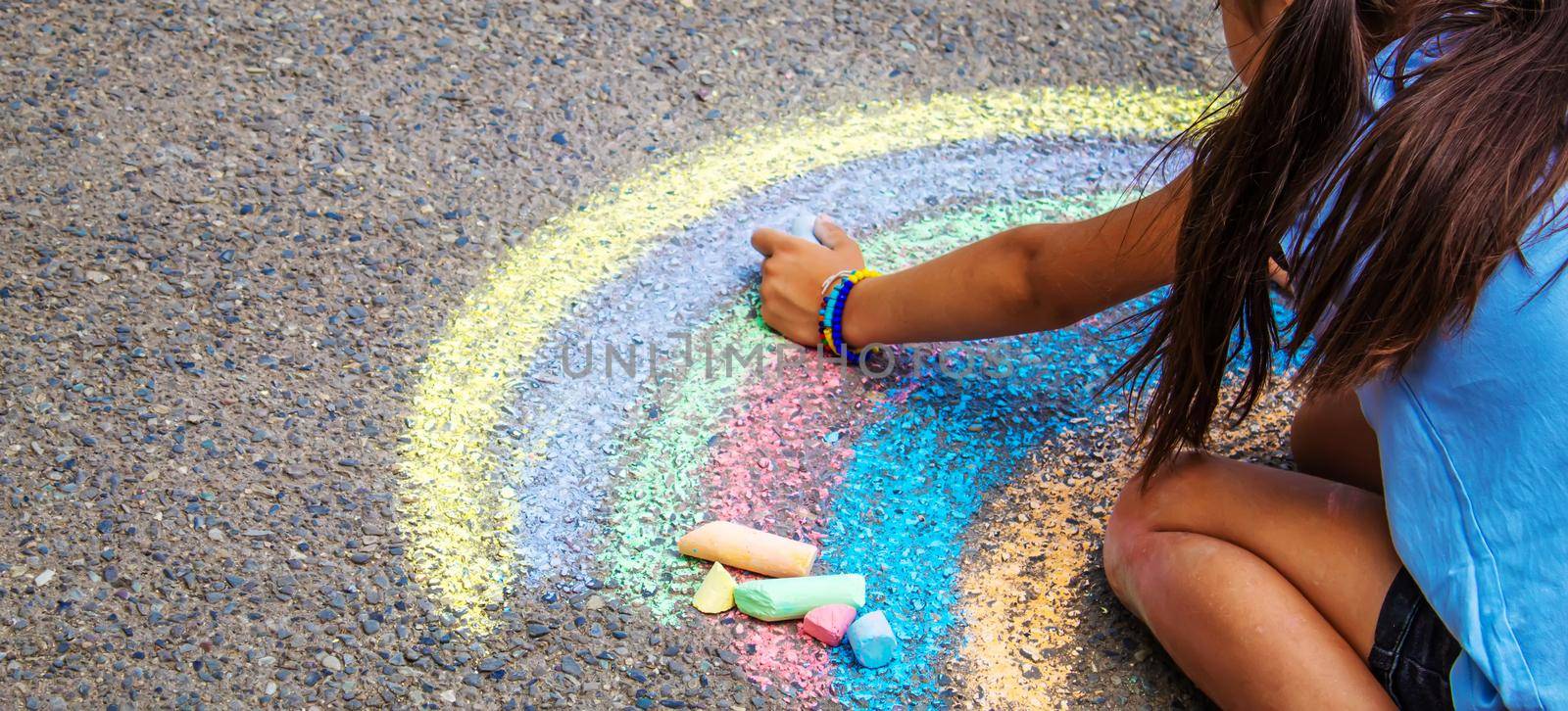 A child draws a rainbow on the asphalt. Selective focus. by mila1784