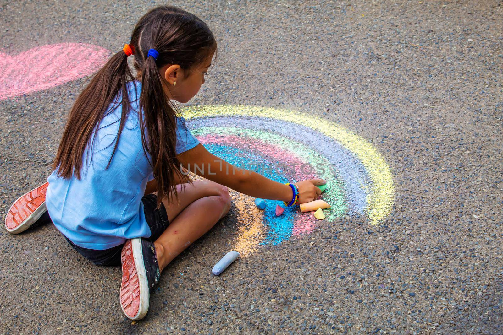 A child draws a rainbow on the asphalt. Selective focus. kid.