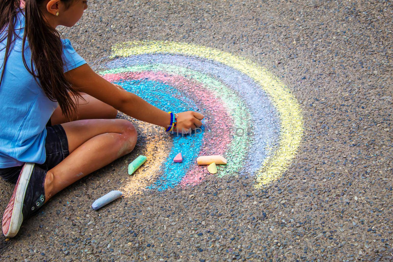 A child draws a rainbow on the asphalt. Selective focus. by mila1784