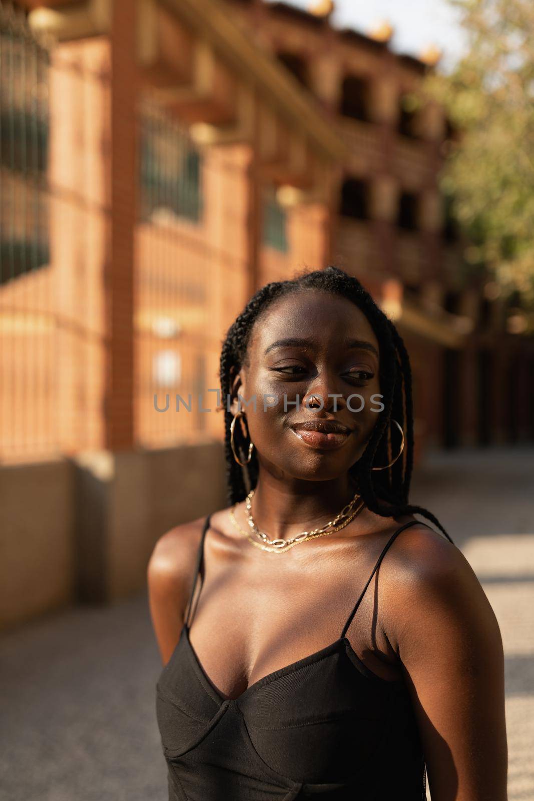 Young black woman posing carefree with her arms behind her back in the street during a beautiful summer sunset