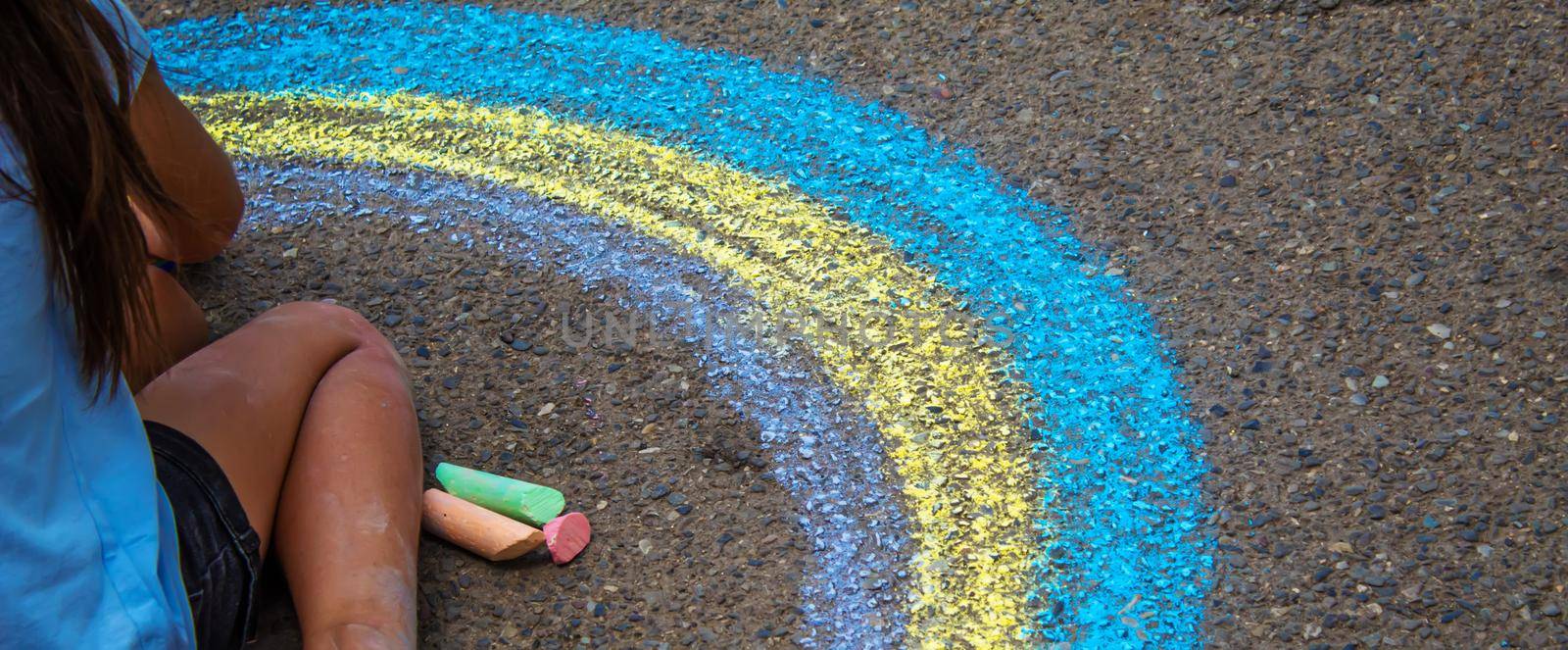 A child draws a rainbow on the asphalt. Selective focus. by mila1784